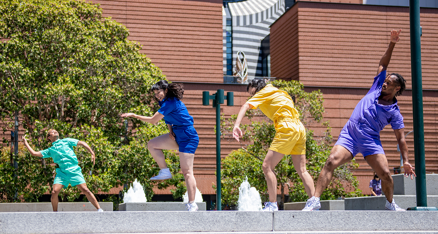 4 dancers in bright colored jumpsuits dance in different poses outdoors