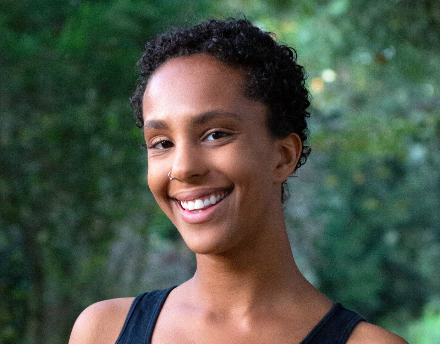 Headshot of Saharla Vetsch, a Somali American woman with short curly black hair smiles in front of a green background. 