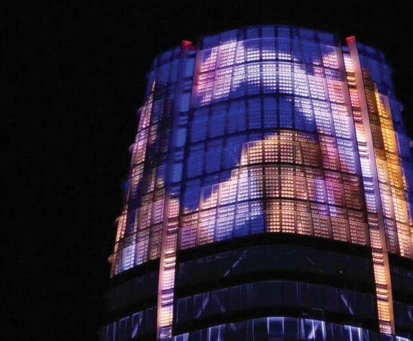 A dance film projected onto the top of a tall building against a night sky.