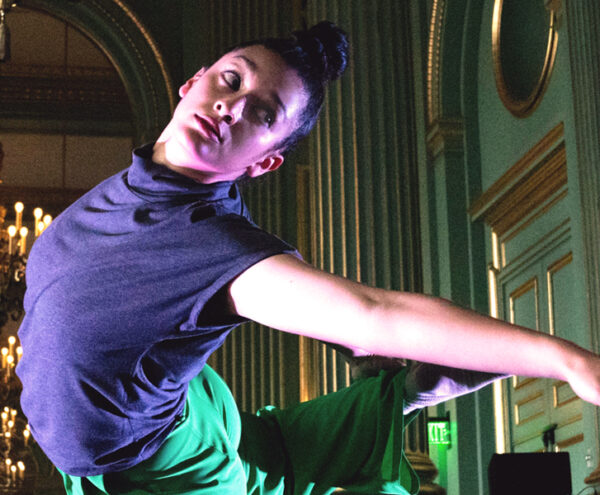 dancer with a high bun reaches and looks to the left in an ornate green room