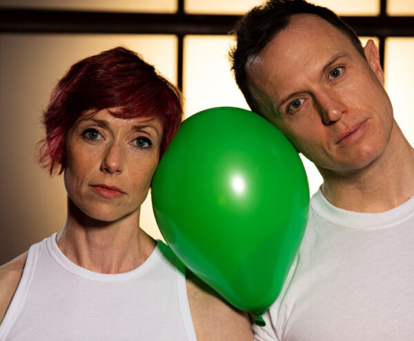 2 dancers rest their heads on a green balloon
