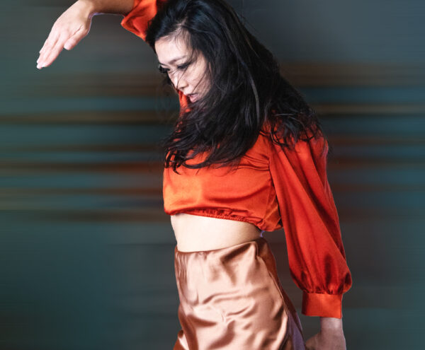 Dancer in orange blouse raises arm at a sharp angle
