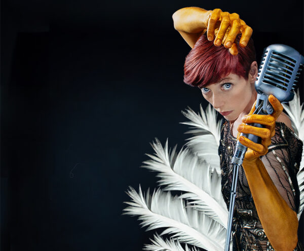 dancer in sequins with gold painted arms holds old fashioned microphone in front of feathers