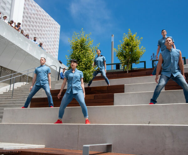 5 dancers in blue outfits and red shoes pose on concrete stairs outdoors